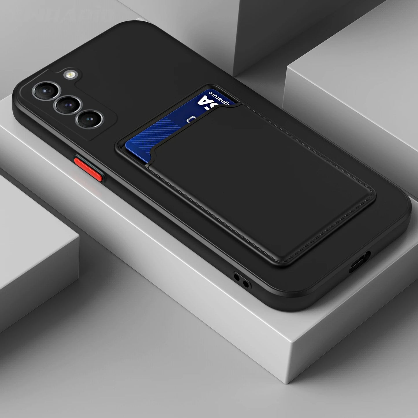 Black phone case with a cardholder pocket displaying a blue card. The case shows three camera lenses and a red button, resting on a gray geometric surface.
