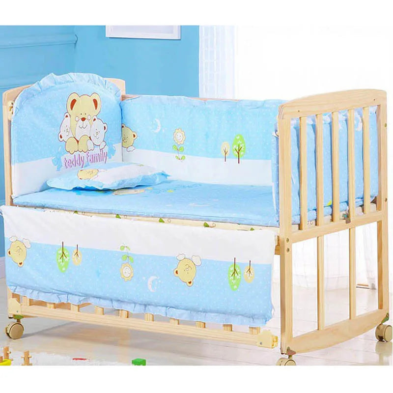 Wooden crib with blue teddy bear-themed bedding, featuring cute bear and tree designs. The crib is on wheels, placed in a light, airy nursery room with toys on the floor.