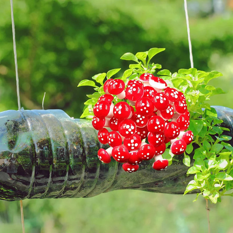 Hanging garden using a recycled bottle with lush green plants growing inside. A cluster of vibrant red and white spotted decorations is attached to the bottle in a green setting.