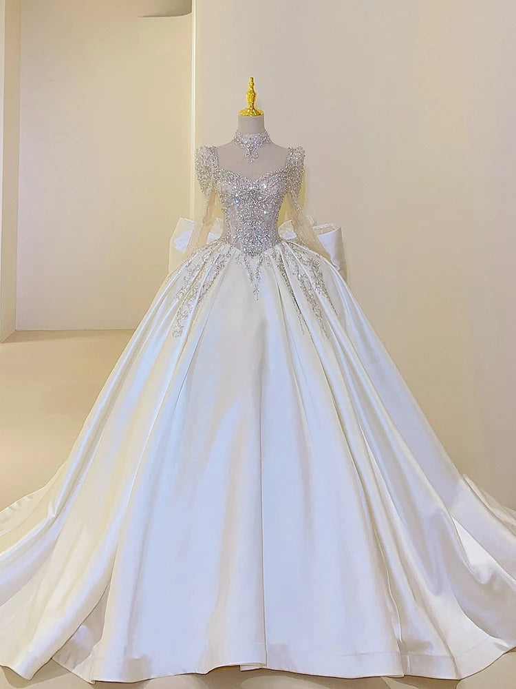 Ornate wedding gown on a mannequin, featuring a full satin skirt and an embellished bodice with intricate lace and crystal details, set against a plain background.