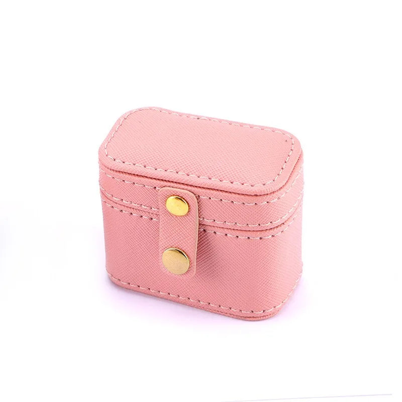 A small pink rectangular jewelry box with a textured surface and yellow snap buttons, designed for portable storage.