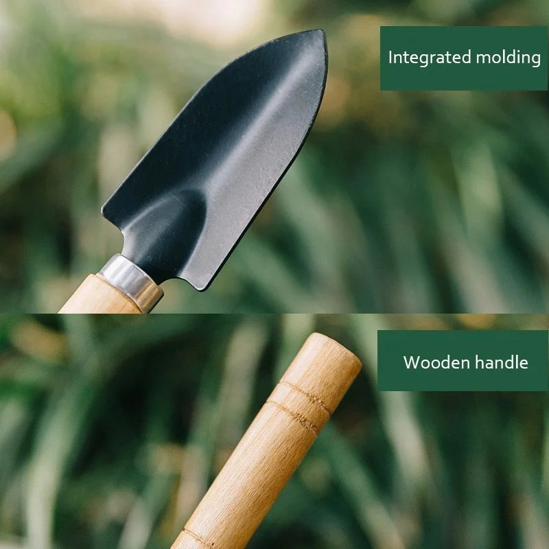 Close-up of a garden trowel with a black integrated molded metal head and a smooth wooden handle. The background is blurred green foliage.