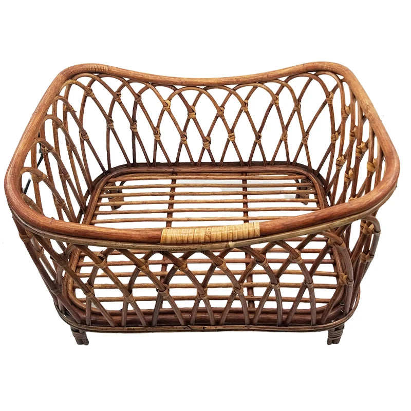 A square, open-weave rattan basket with reinforced edges, featuring a crisscross pattern and a slatted base. The basket is light brown and has a natural, rustic appearance.