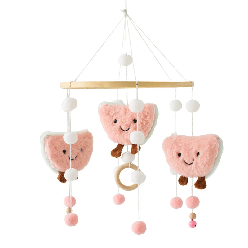 A baby mobile with plush, smiling pink tacos and white pom-poms hanging from a wooden hoop. Each taco has brown feet, adding a playful touch to the nursery decor.