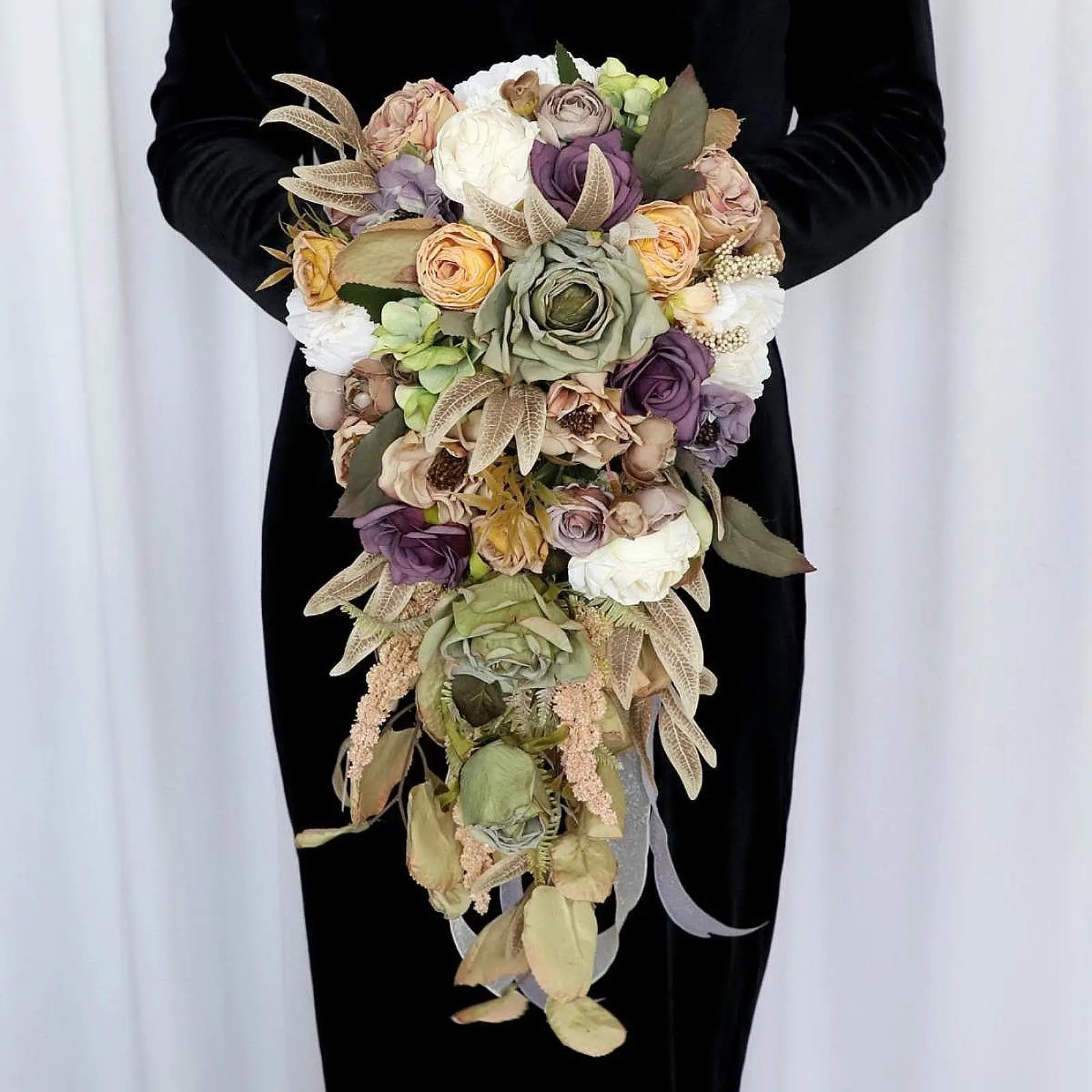 A person holds a cascading bouquet with roses and greenery in purple, white, and beige tones against a black dress.