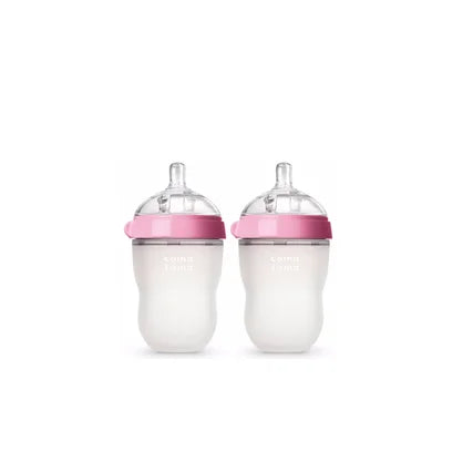 Two baby bottles with pink lids and clear nipples, side by side against a white background. The bottles have a wide neck and are marked with measurement lines.
