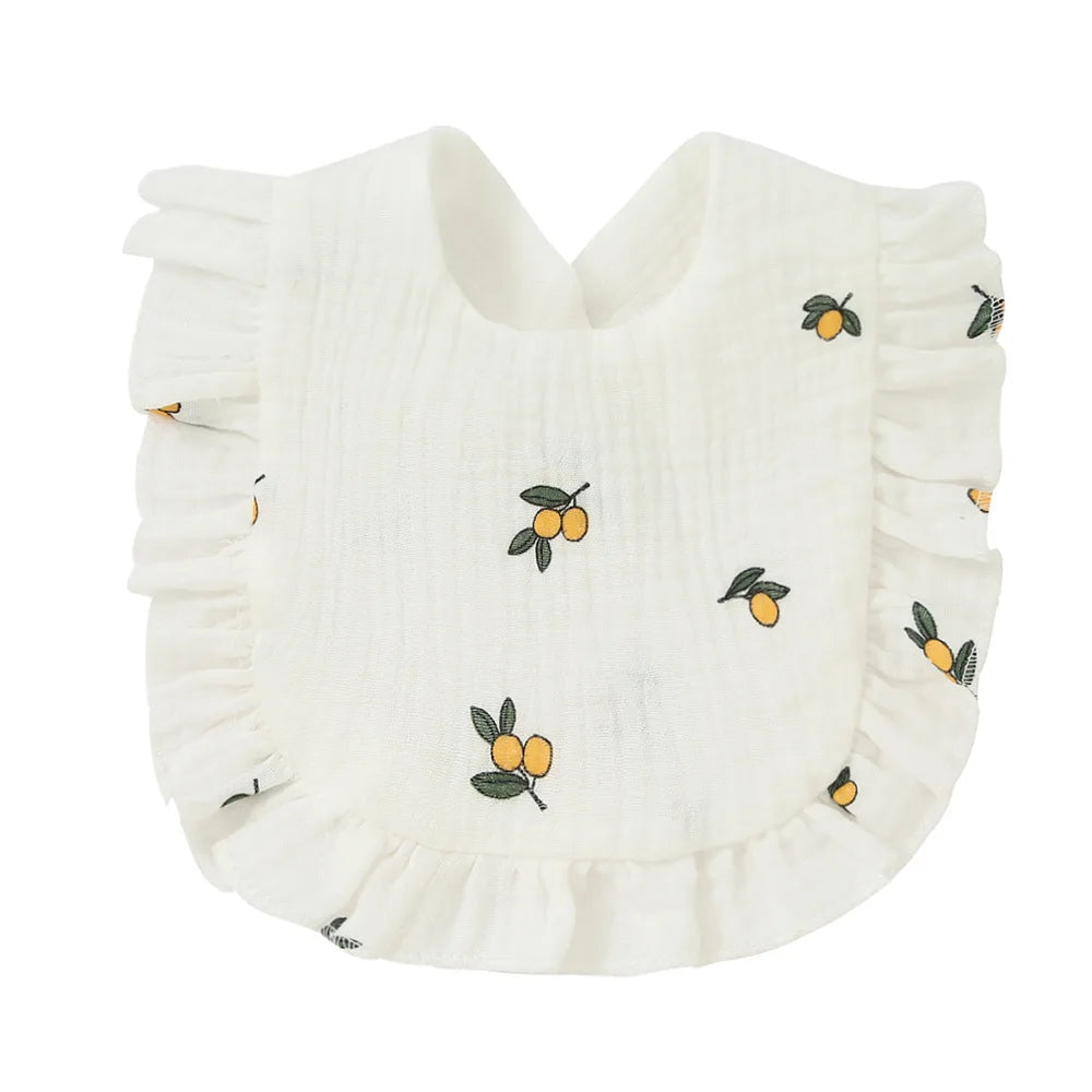 White baby bib with small orange fruit print and leafy accents, featuring a soft ruffled edge.