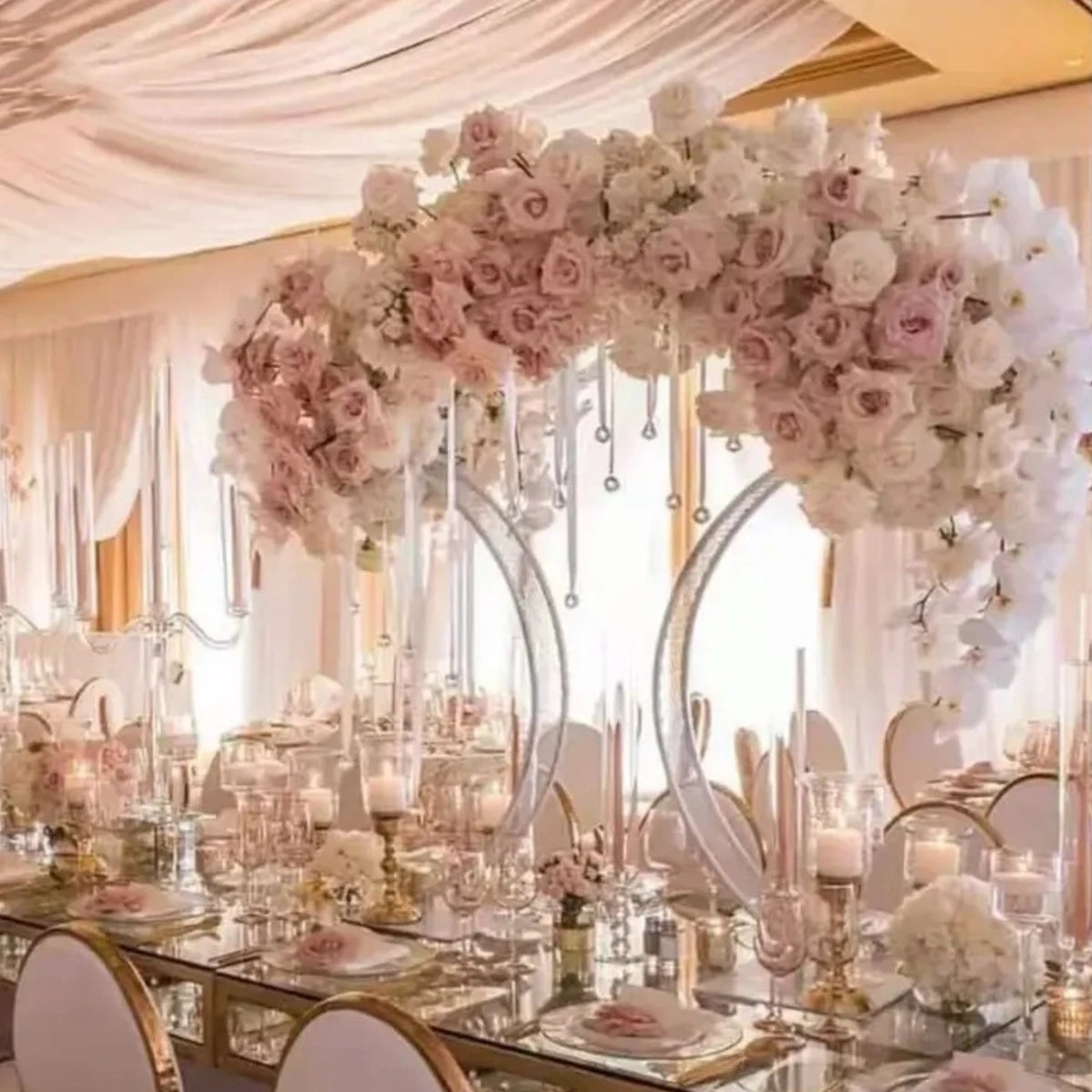 Elegant wedding table with a mirrored top, adorned with pink and white floral arrangements, tall taper candles, and draped fabric ceiling, creating a luxurious atmosphere.