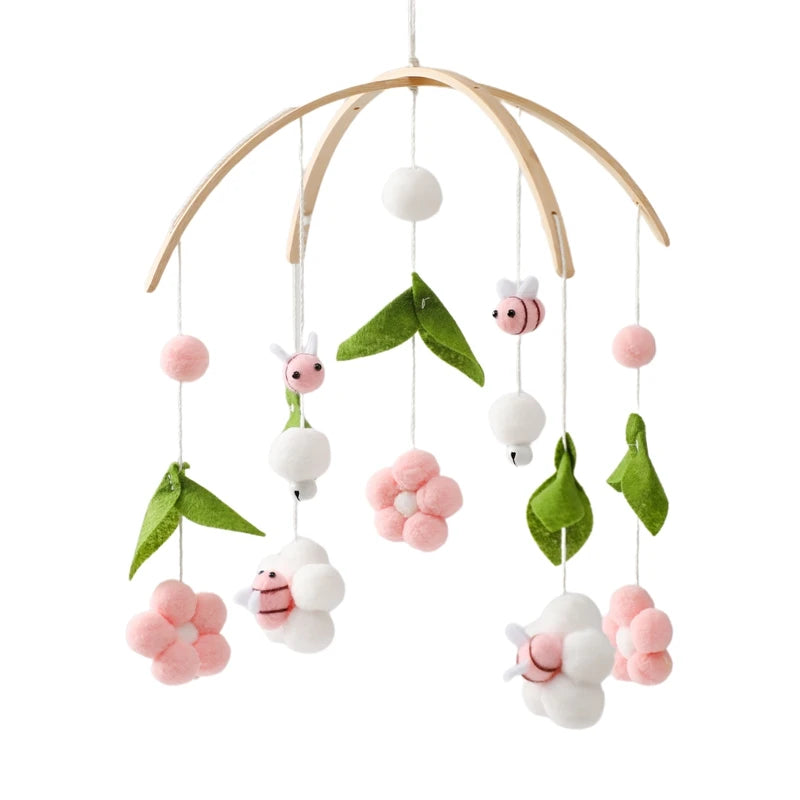 Wooden baby mobile with felt flowers, leaves, and bees in pink, white, and green. Each piece dangles delicately from the wooden frame, creating a whimsical nursery decoration.