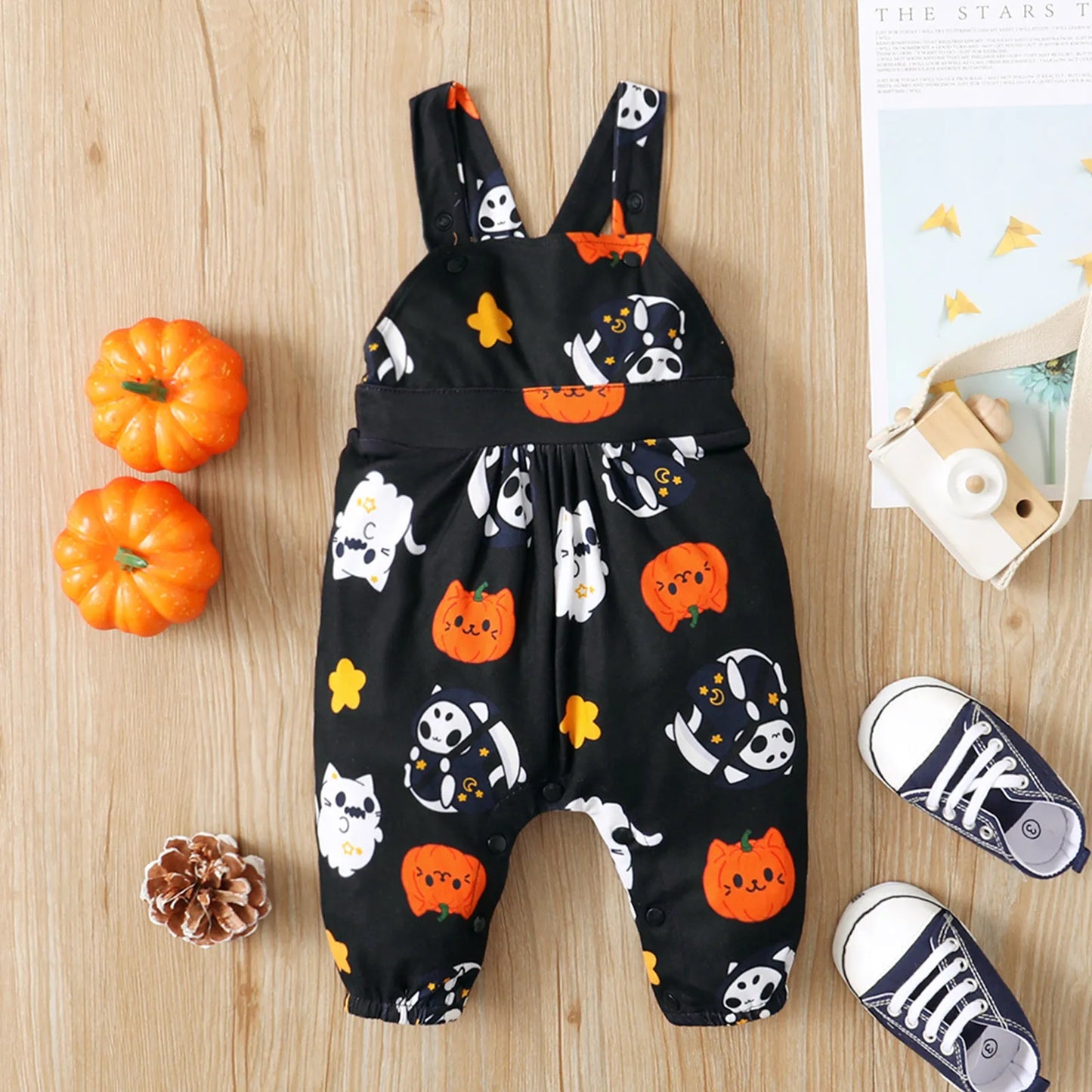A baby's Halloween-themed romper with playful pumpkin and ghost prints, laid on a wooden floor. Nearby are two mini pumpkins, a pine cone, a toy camera, and baby shoes.