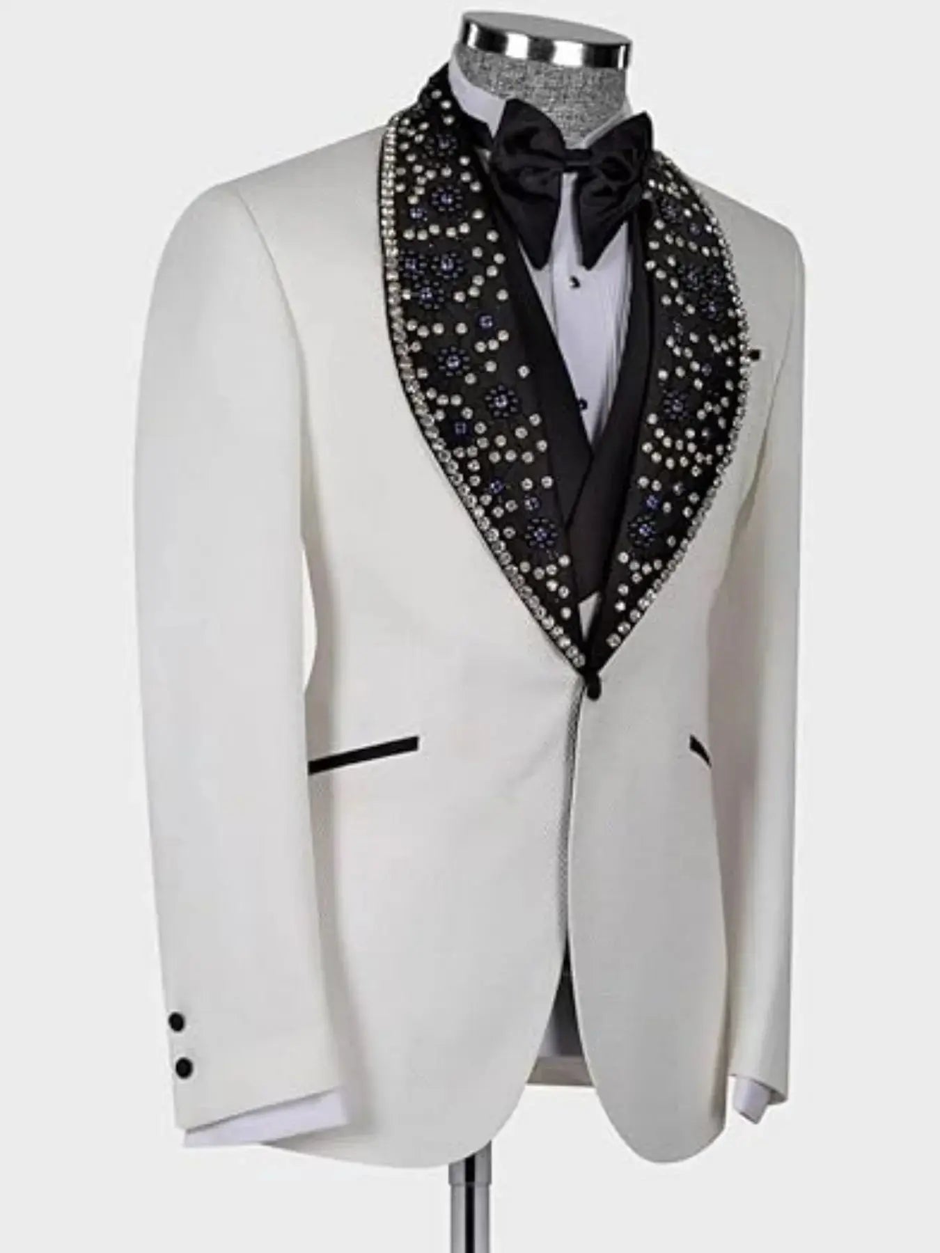 Elegant white tuxedo with a black, jewel-studded shawl lapel on a mannequin. Features a black bow tie and contrasting black piping on the pockets and sleeves.