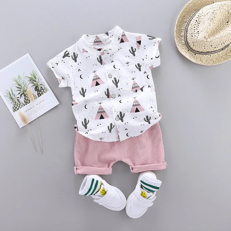 Children's summer outfit includes a white shirt with black and pink teepee and cactus print, pink shorts, white sneakers with smiley faces, and a straw hat.