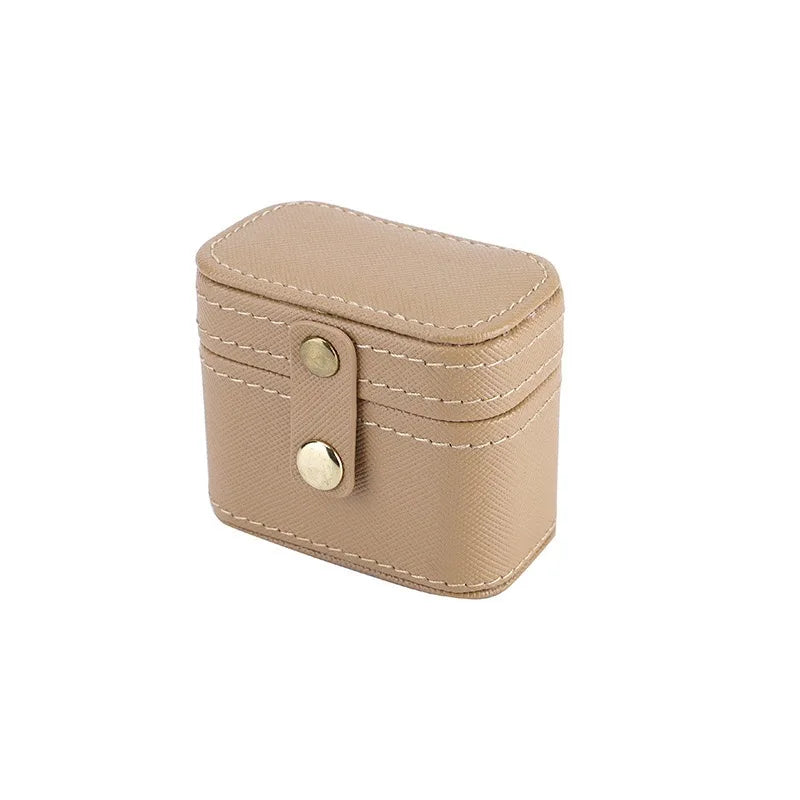 Small beige leather box with rounded corners and white stitching, featuring a snap closure with two gold buttons on the front, designed for compact storage or travel.
