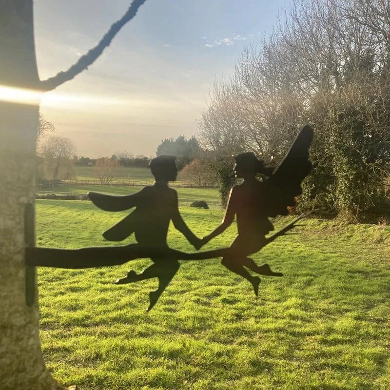 Silhouettes of two fairies holding hands, perched on a branch against a sunlit countryside backdrop with lush green grass and bare trees under a partly cloudy sky.