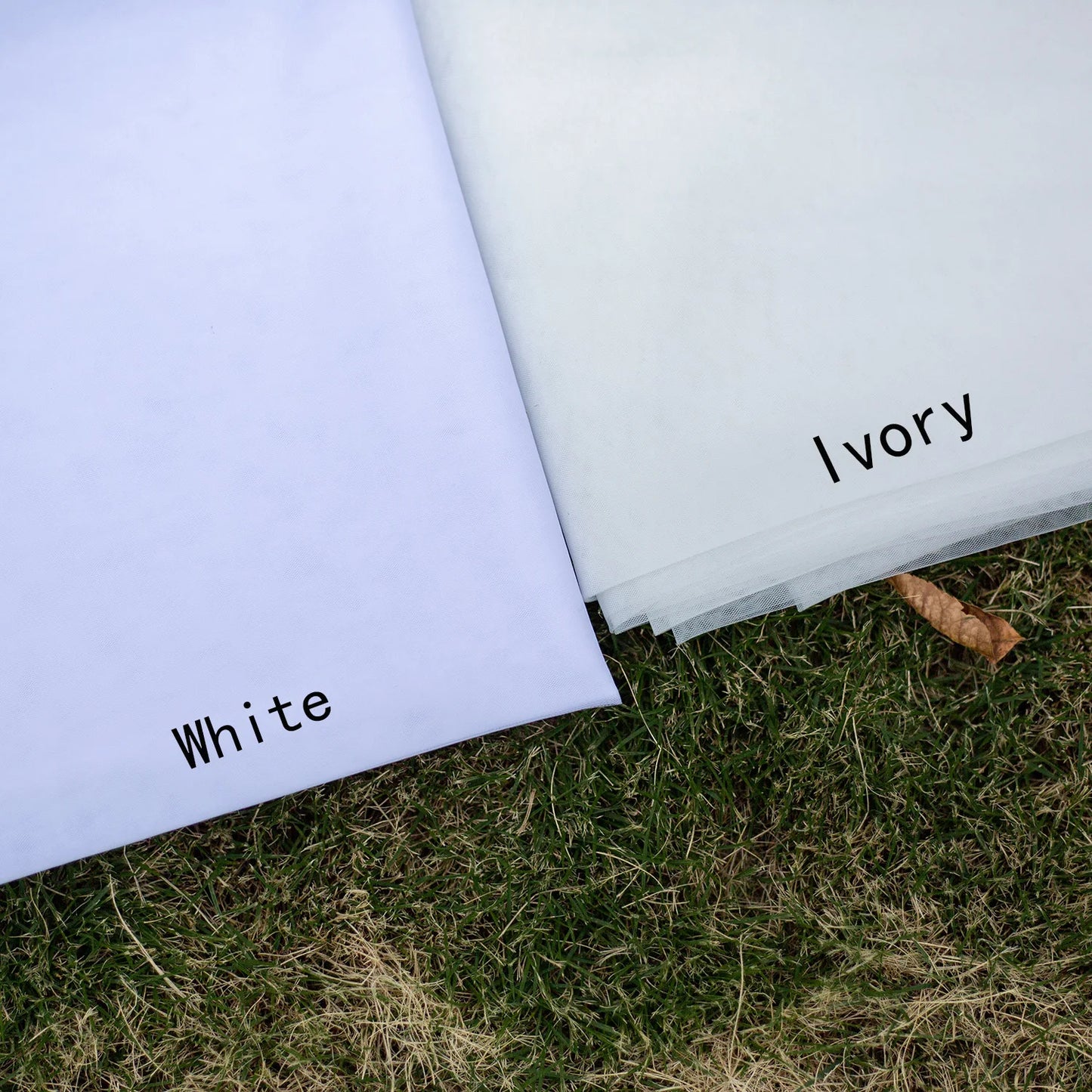 Two fabric sheets labeled "White" and "Ivory" are displayed on grass, showcasing subtle color differences.