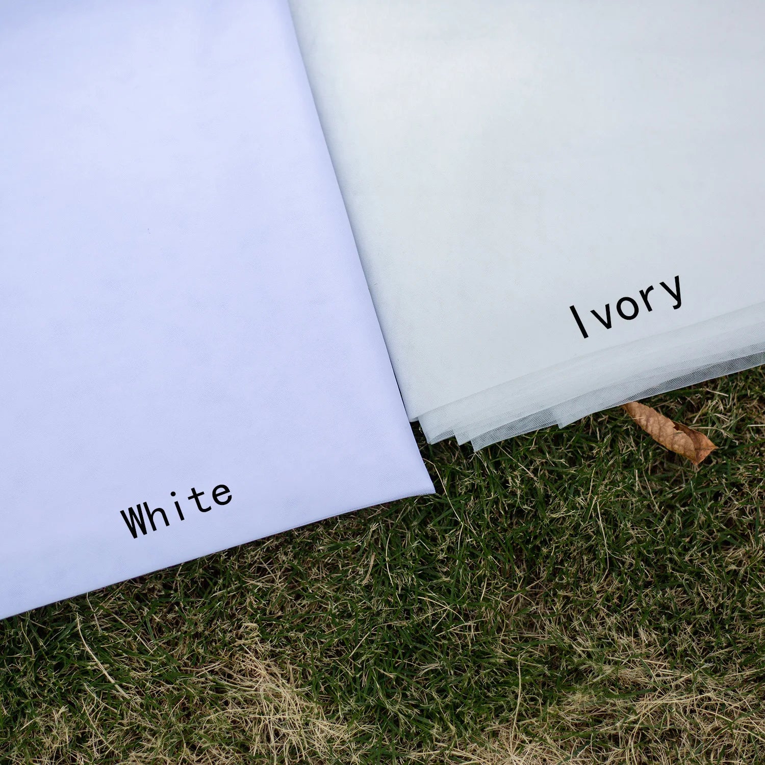 Two fabric sheets labeled "White" and "Ivory" are displayed on grass, showcasing subtle color differences.