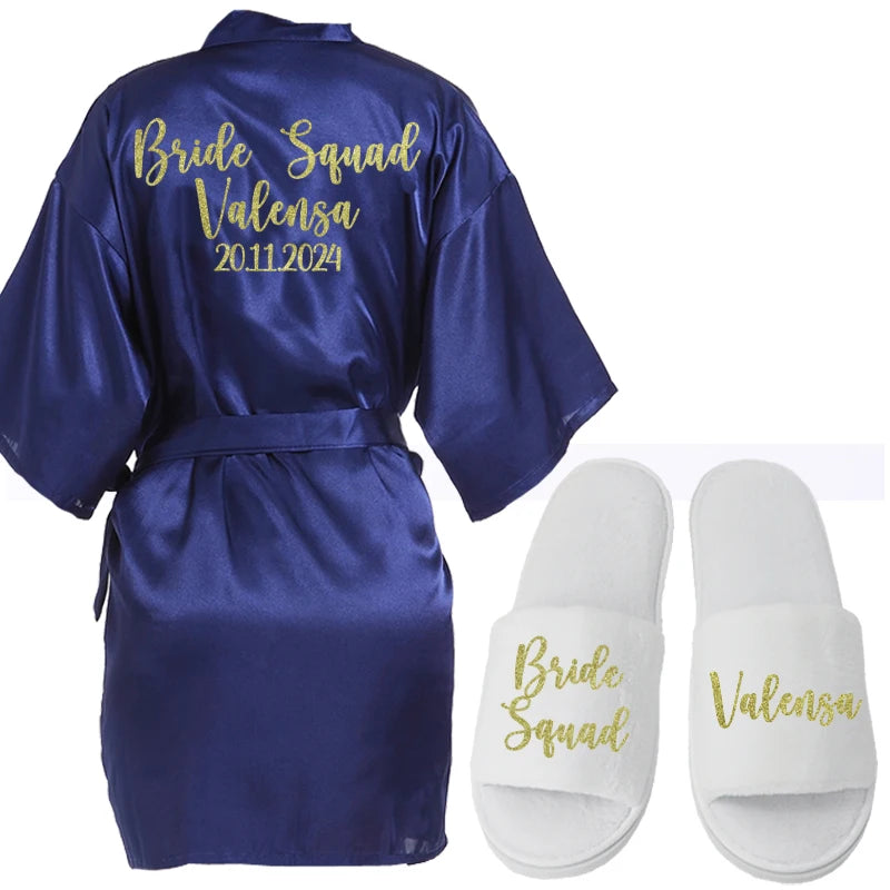 Navy satin robe with "Bride Squad Valensa 20.11.2024" in gold script, paired with white slippers. Slippers are adorned with "Bride Squad" and "Valensa" in matching gold lettering.