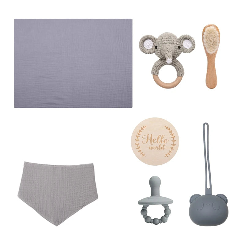 A baby gift set includes a gray blanket, elephant teether, baby brush, "Hello world" disc, gray bib, pacifier with beads, and a bear-shaped case.
