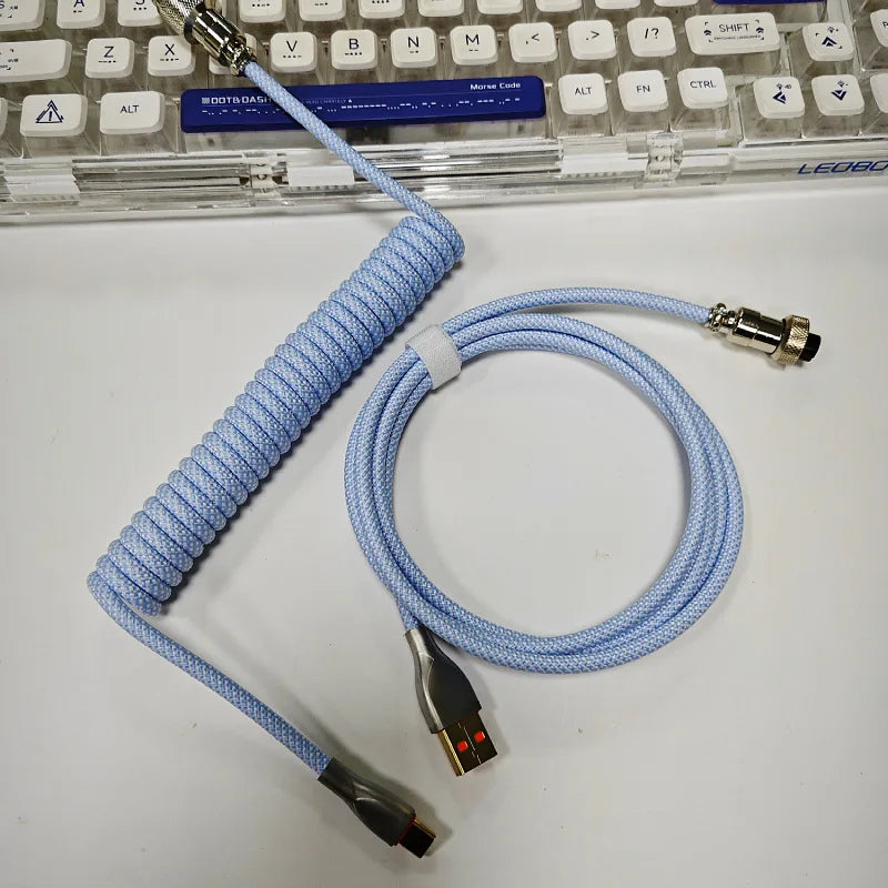 Coiled blue keyboard cable with USB and metal connectors lies on a white surface, next to a clear keyboard with white keys.