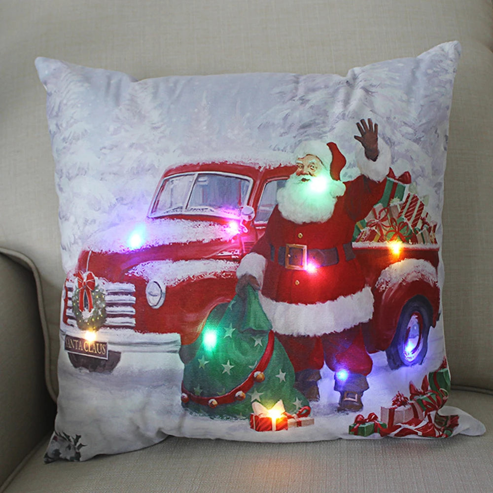 Cushion with a festive scene of Santa beside a red truck with gifts, featuring colorful LED lights on snow-covered ground.