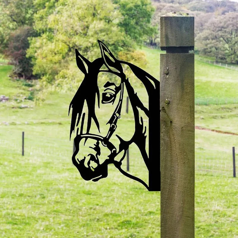Metal horse silhouette attached to a wooden post stands in a lush, green field with rolling hills and trees in the background.