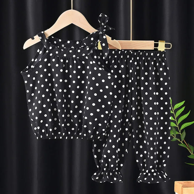 Black polka dot toddler outfit with a sleeveless top and matching pants, hanging on a wooden hanger. The top features tied shoulder straps and the pants have gathered hems.