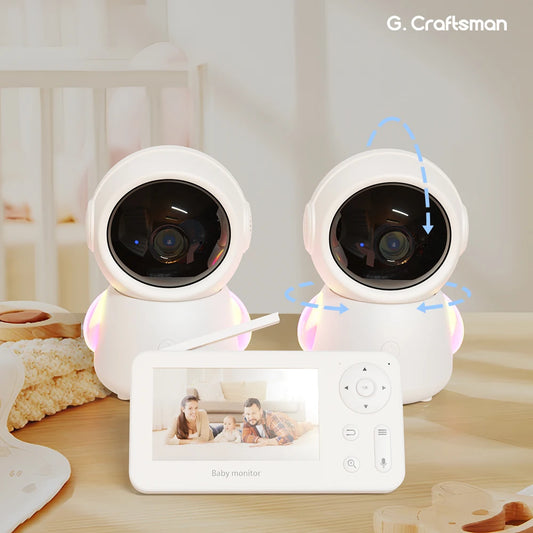 Two white baby monitor cameras with rotatable lenses are placed on a table, alongside a separate display screen showing a family. The brand name "G. Craftsman" is visible above.