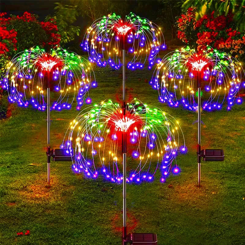 Four LED garden lights in vibrant colors of red, green, and purple, arranged like glowing dandelions, illuminate a lush garden at night with solar panels visible.