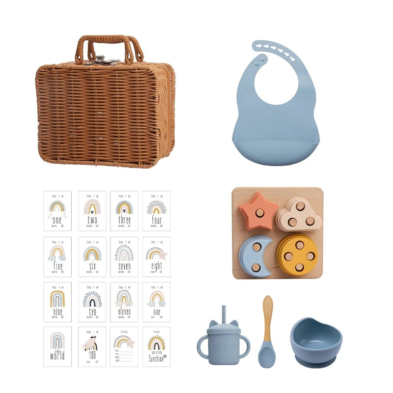 Wicker basket set with silicone bib, milestone cards, wooden puzzle, sippy cup with straw, bamboo spoon, and silicone bowl, all in soft, neutral colors.