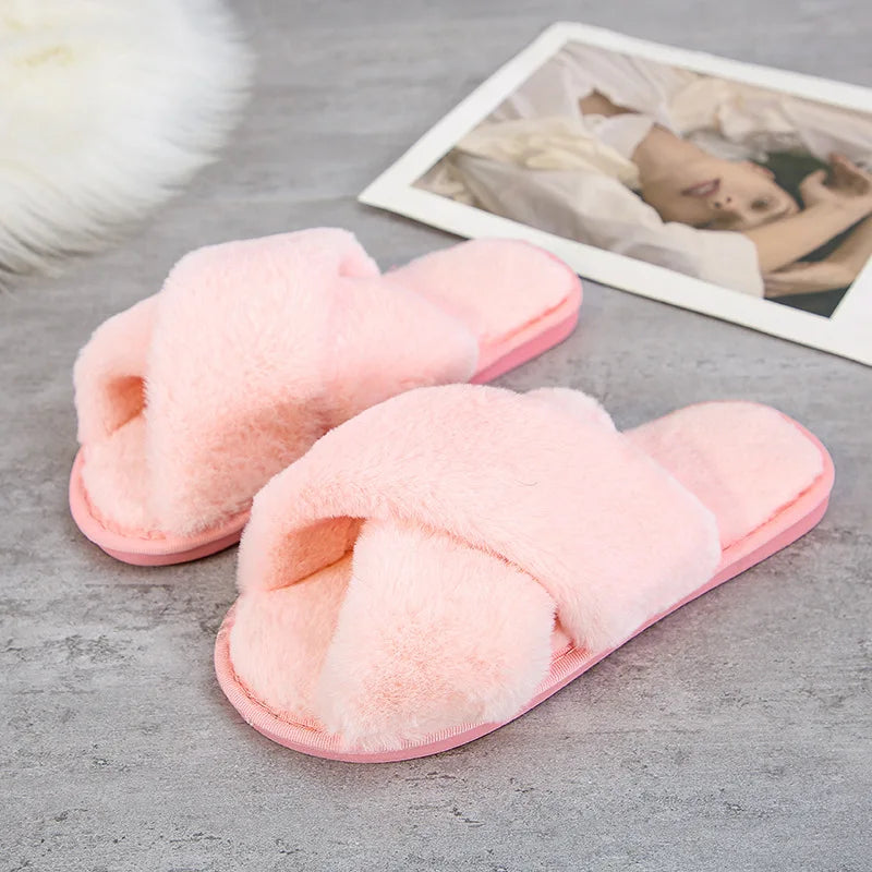 Soft pink fuzzy slippers with crisscross straps are placed on a gray surface. A photo of a person wearing white is partially visible in the background.