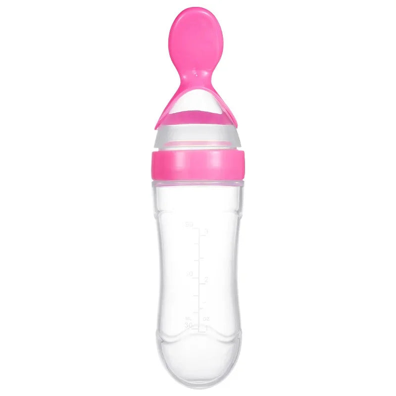 Clear baby bottle with pink cap and spoon attachment, featuring measurement marks on the side.
