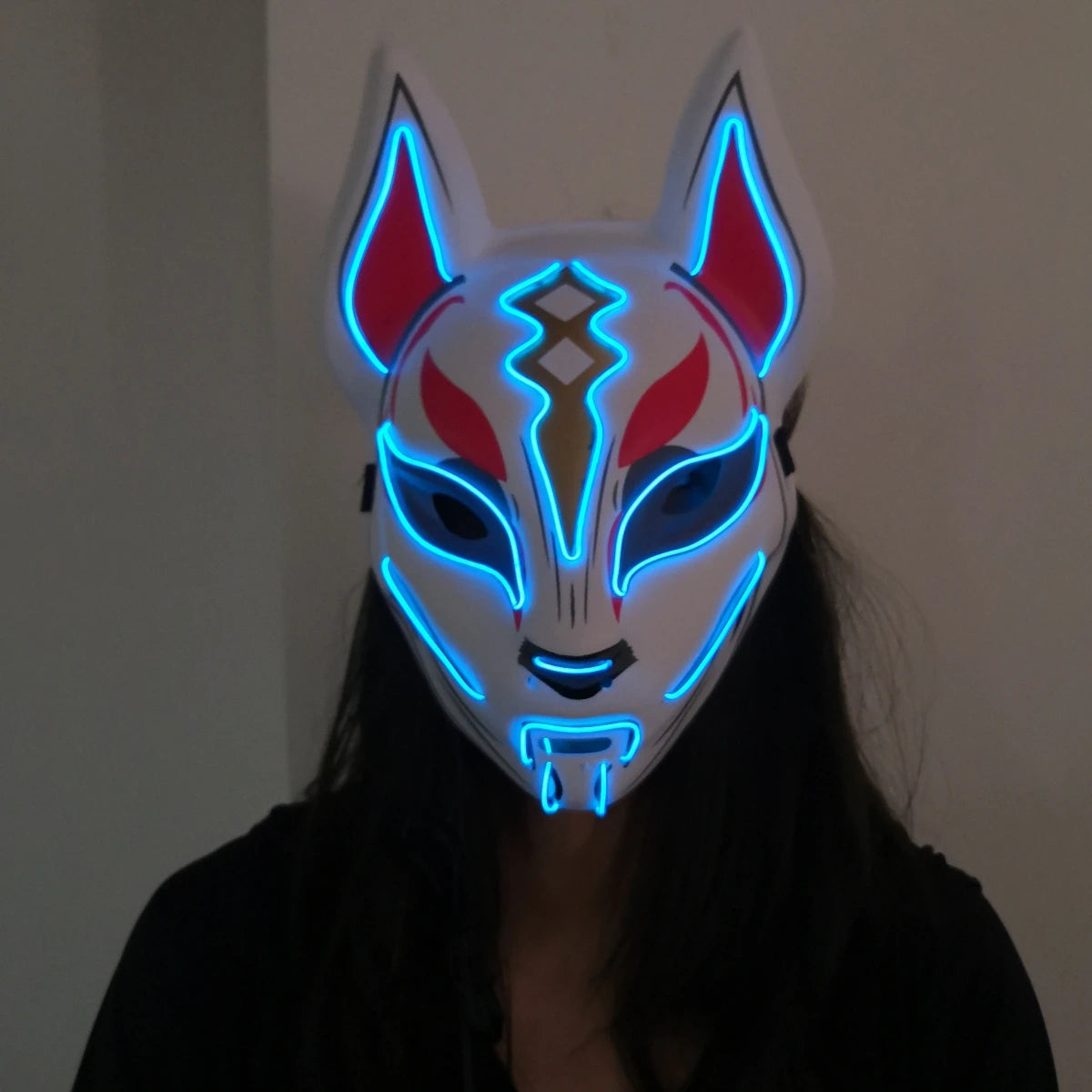 Person wearing a white fox mask with glowing blue outlines and red accents, featuring pointed ears and geometric patterns, set against a plain background.