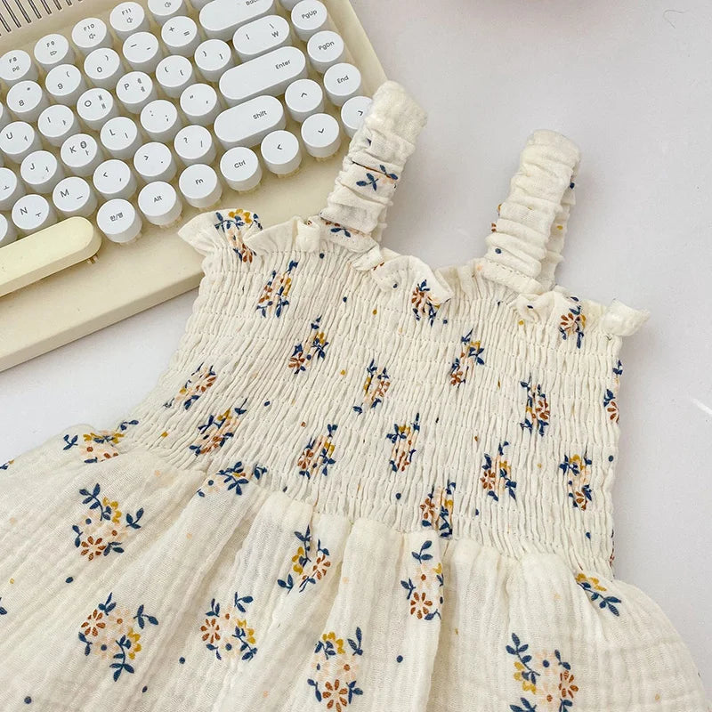 A white smocked dress with blue and yellow floral patterns lies alongside a white keyboard with round keys, creating a soft and minimalistic aesthetic.