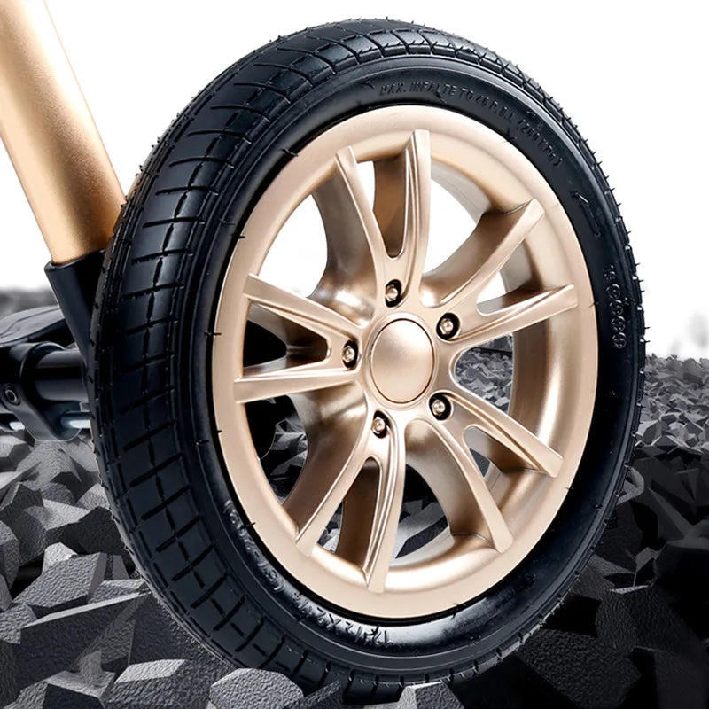 Close-up of a shiny gold alloy wheel with a black tire on rough, textured ground. The design features five dual spokes and visible lug nuts.