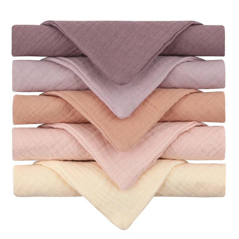 Stack of six folded cloths in soft pastel shades, including lavender, peach, and cream. Each is arranged neatly with corners overlapping, showcasing texture and color.