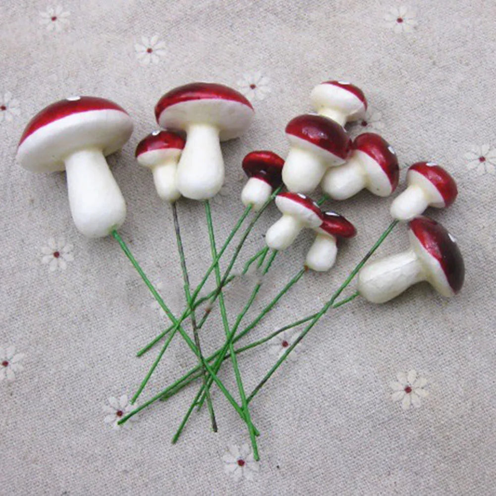 Artificial red and white mushrooms with green wire stems arranged on a textured fabric background with small floral designs.