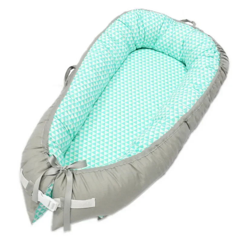 Gray and mint baby nest with geometric patterned lining. It features soft, padded sides and securing straps at the bottom, providing a cozy space for an infant.