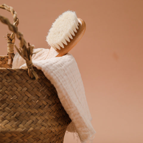 Basket with a textured towel and a wooden exfoliating brush with white bristles against a beige background. The woven basket and soft cloth evoke a spa-like atmosphere.