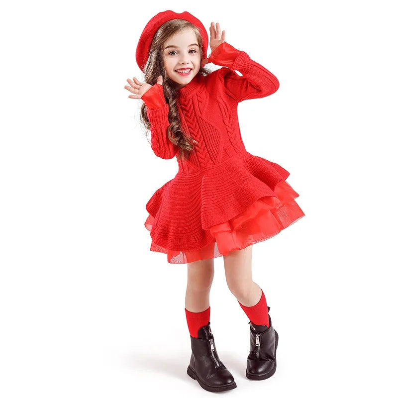 Young girl posing playfully in a bright red knitted dress with a tiered skirt, matching beret, and black ankle boots, set against a plain white background.