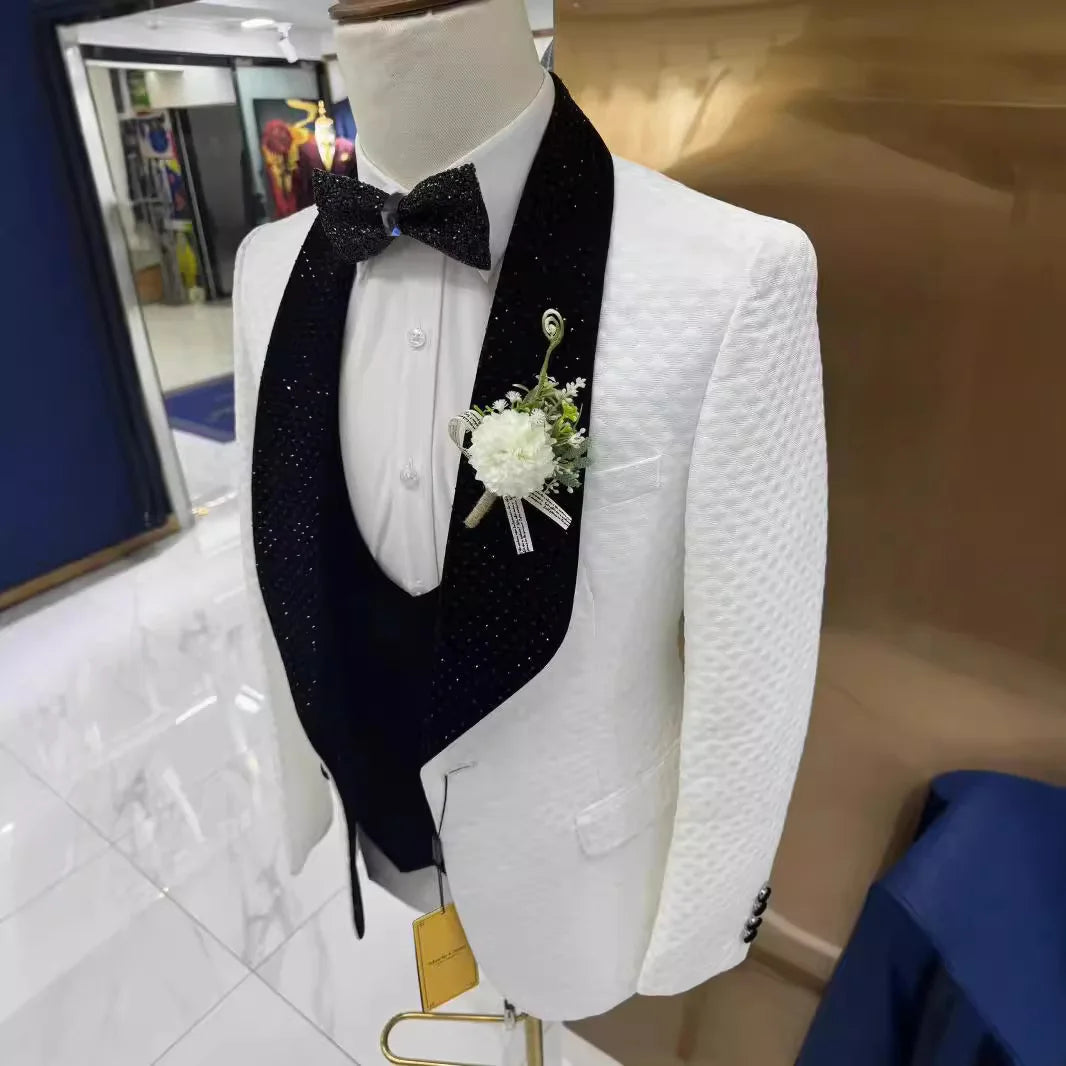 A mannequin displays a white textured tuxedo with a black, sparkling lapel and bow tie, complemented by a white floral boutonniere. The setting includes a glossy floor.