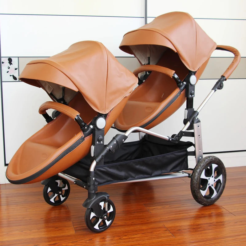 Double stroller with tan leather seats and canopies, placed indoors on a wooden floor. It features four wheels and a black storage basket beneath.
