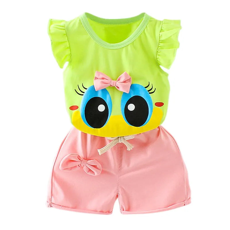 Cute children's outfit featuring a green top with a cartoon face and pink bow, paired with pink shorts tied at the waist with a bow. The top has ruffled sleeves.