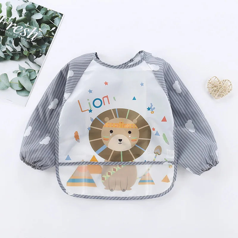 Gray and white bib with long sleeves, featuring a cute lion and colorful shapes. The words "Lion" are written above the lion. A magazine and heart decor lie nearby.