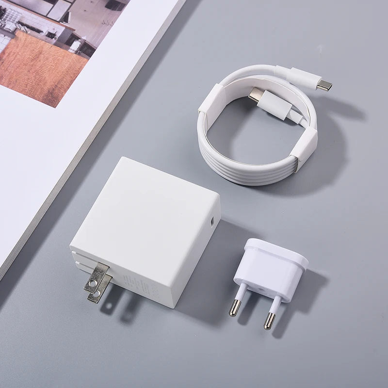 White USB-C charging cable, power adapter with foldable prongs, and Euro plug adapter on a gray surface beside a corner of an open magazine.