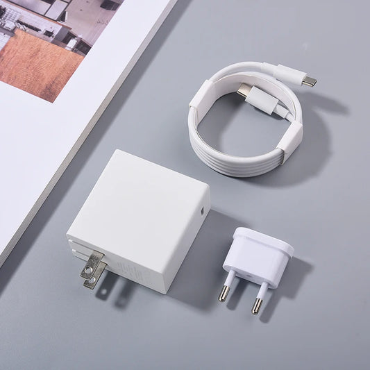 White USB-C charging cable, power adapter with foldable prongs, and Euro plug adapter on a gray surface beside a corner of an open magazine.