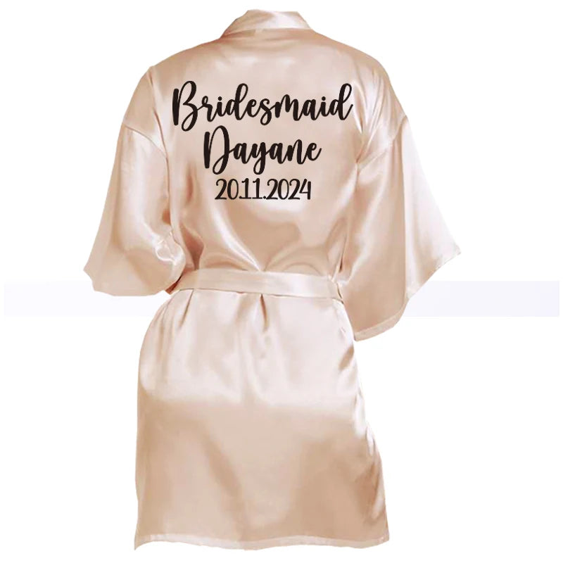 Silky beige robe with "Bridesmaid Dayane 20.11.2024" written on the back in black script. The robe has a waist tie and loose-fitting sleeves.