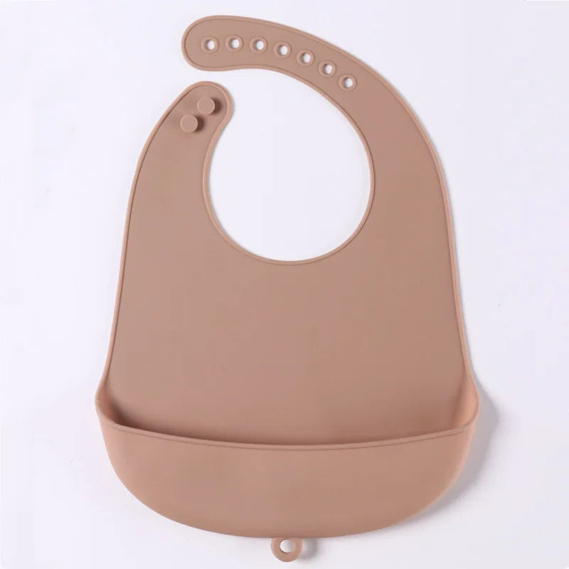 A beige silicone bib with adjustable snaps and a wide pocket at the bottom, designed to catch food spills. Perfect for toddlers during messy meals.