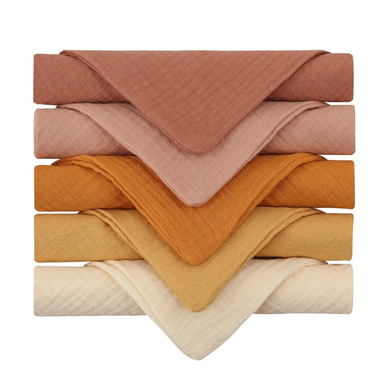 Stack of six folded cloths in brown, soft pink, two shades of orange, mustard yellow, and cream. Each is arranged to show a neat, layered look.
