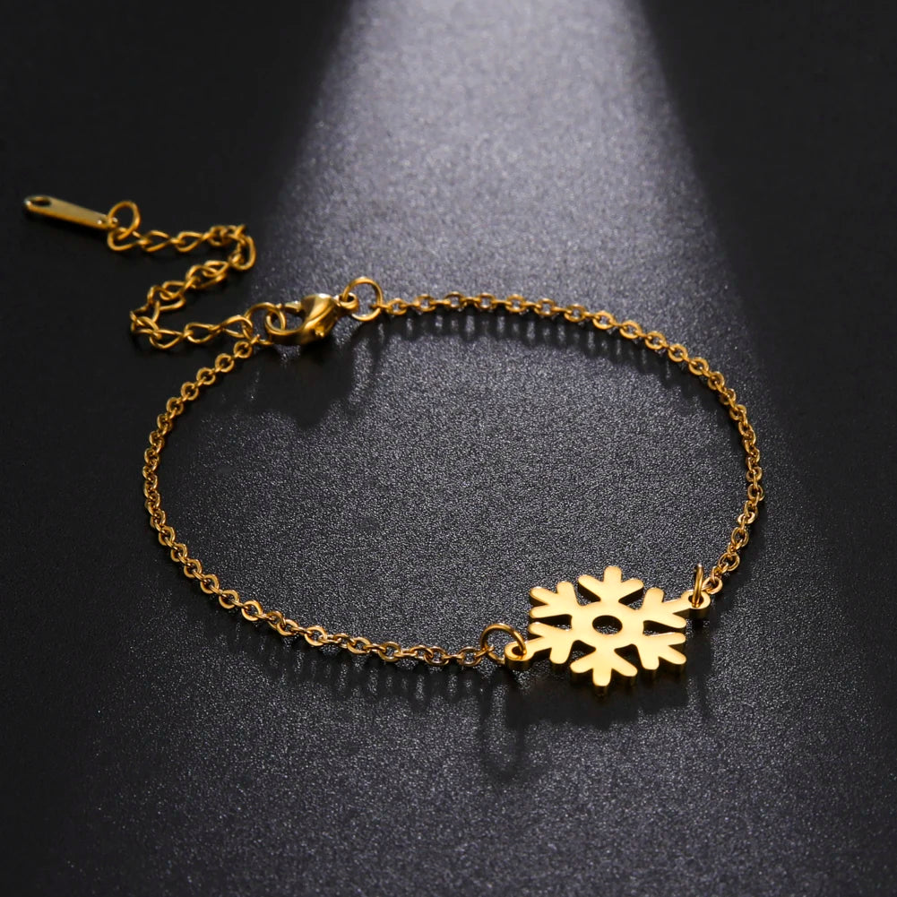 Gold chain bracelet with a snowflake charm displayed on a dark surface. The chain features an adjustable clasp, and the snowflake is centered under a soft spotlight.