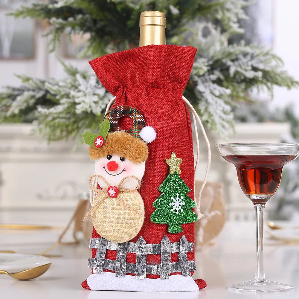 A wine bottle in a festive red cover adorned with a cheerful snowman, green tree, and plaid accents sits beside a glass of red wine against a snowy background.